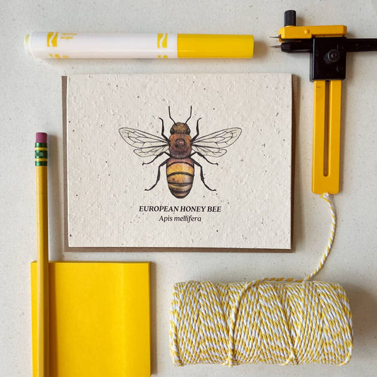 Notebook with bee illustration, yellow pen, and spool of thread on a light background