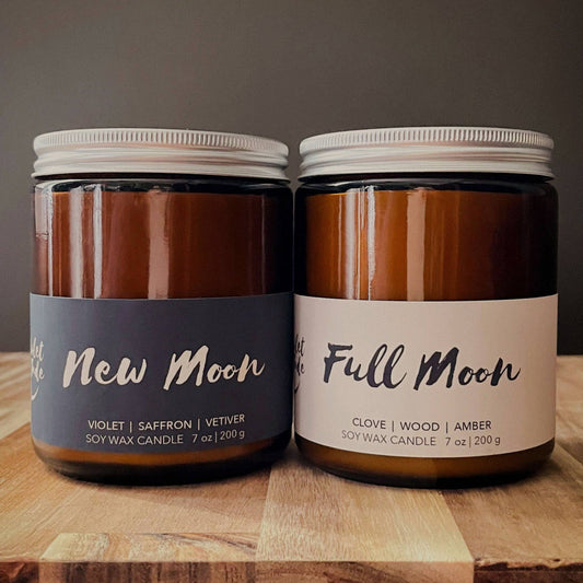 Two candles labeled 'New Moon' and 'Full Moon' on a wooden surface with a dark background.