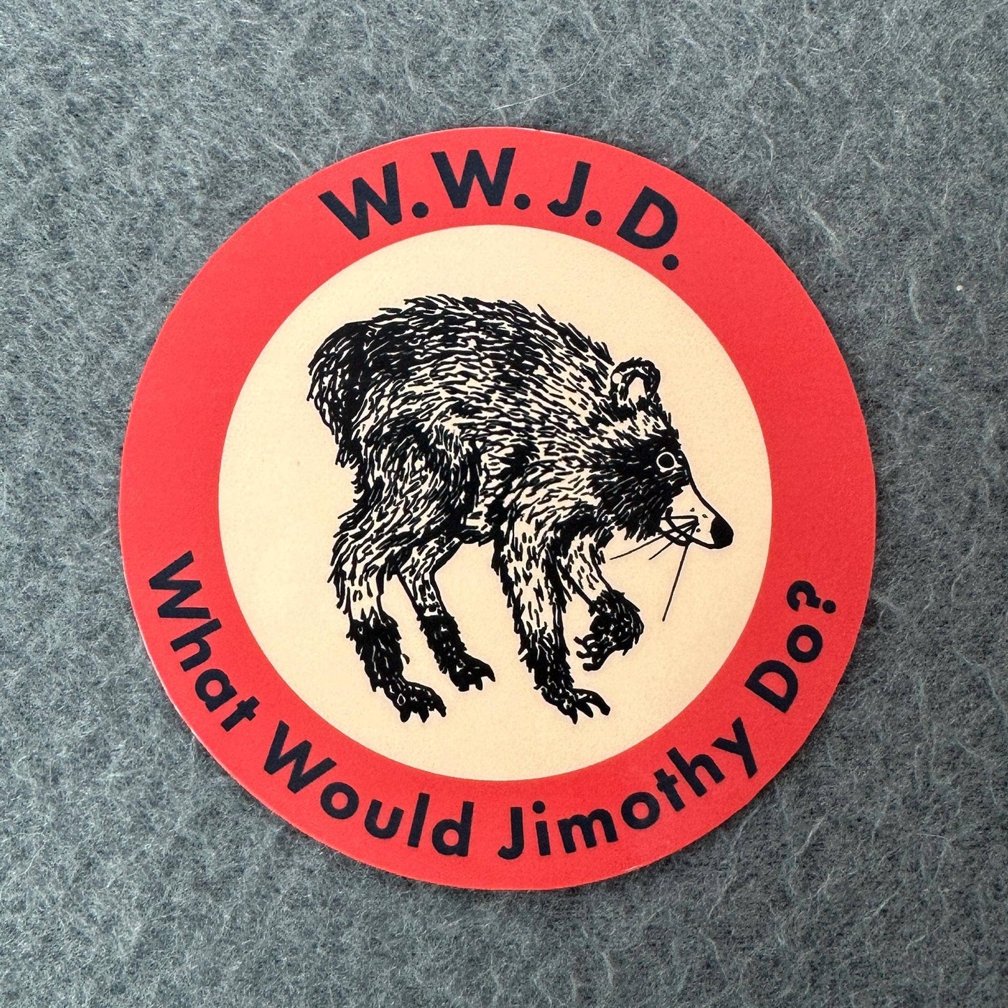 A circular sticker with a red outer border, cream center, and black illustration of a bear holding a twig. The text reads 'W.
