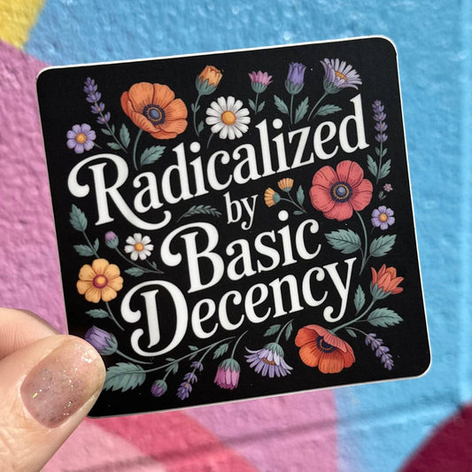 Sticker with floral design and text 'Radicalized by Basic Decency' held against a colorful background.