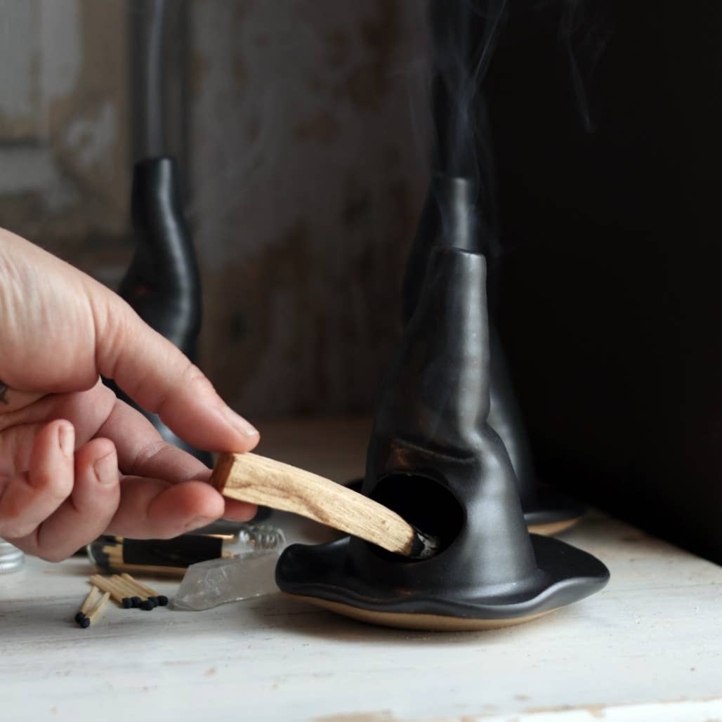 Person placing a stick into a black witch hat-shaped container on a marble surface.