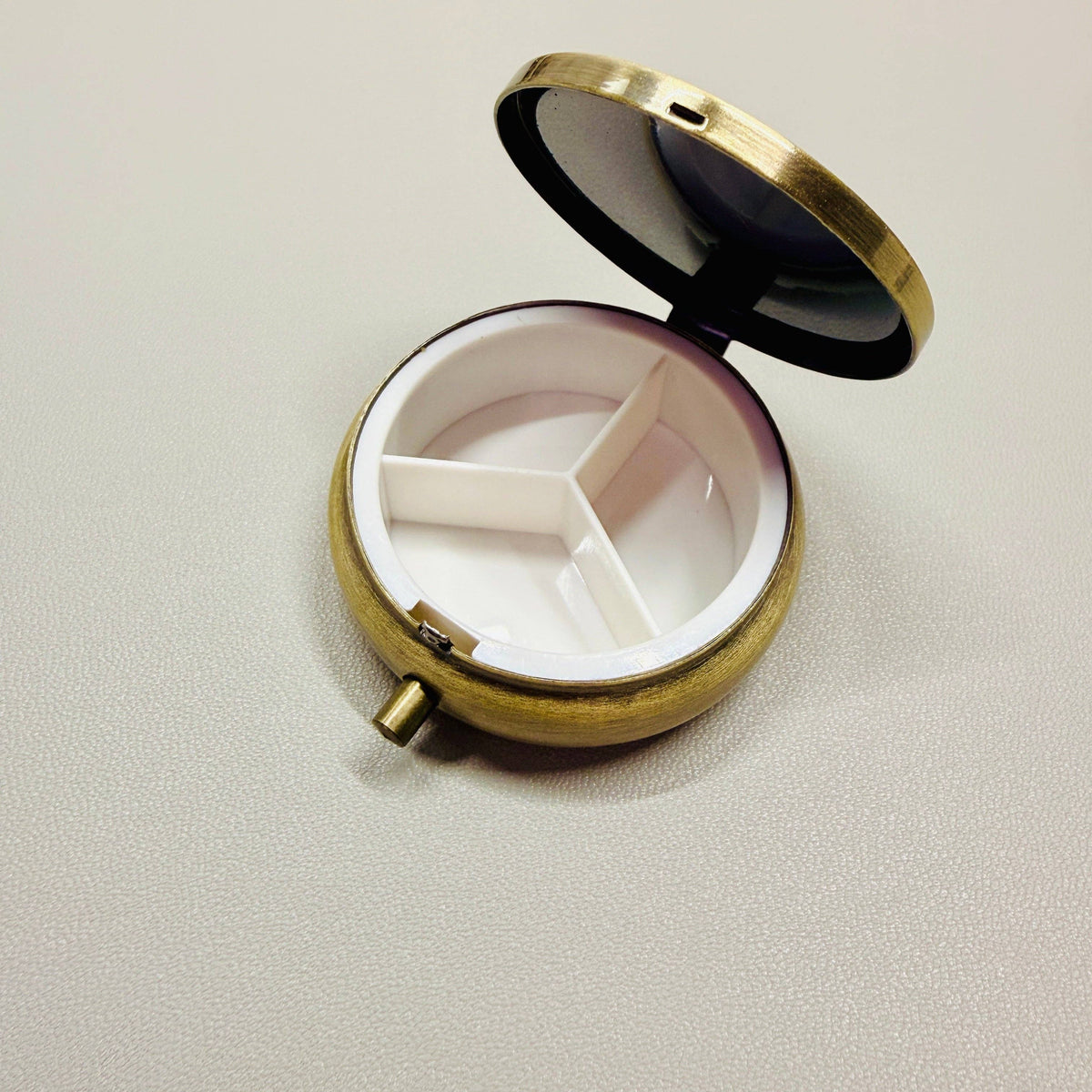Round brass pill box with white interior on a light gray background