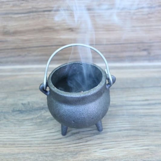 Small black cauldron with smoke on a wooden surface