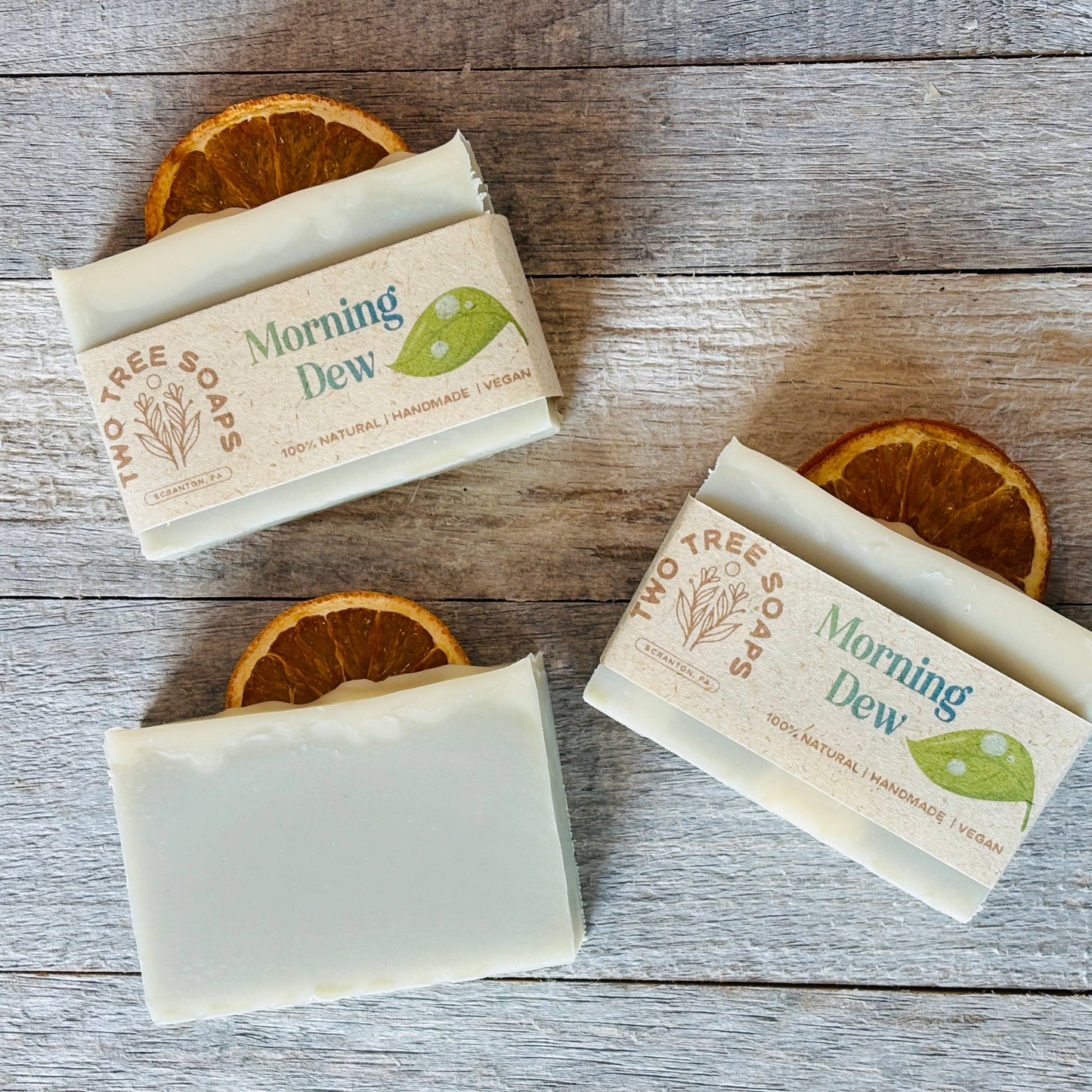 Three bars of 'Morning Dew' soap on a wooden surface with orange slices.