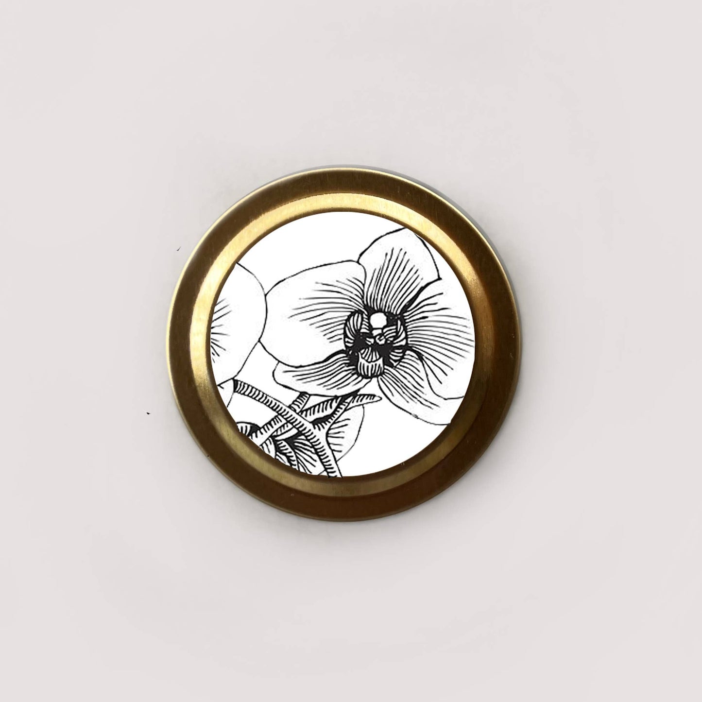 Round brass object with black and white floral design on a light gray background