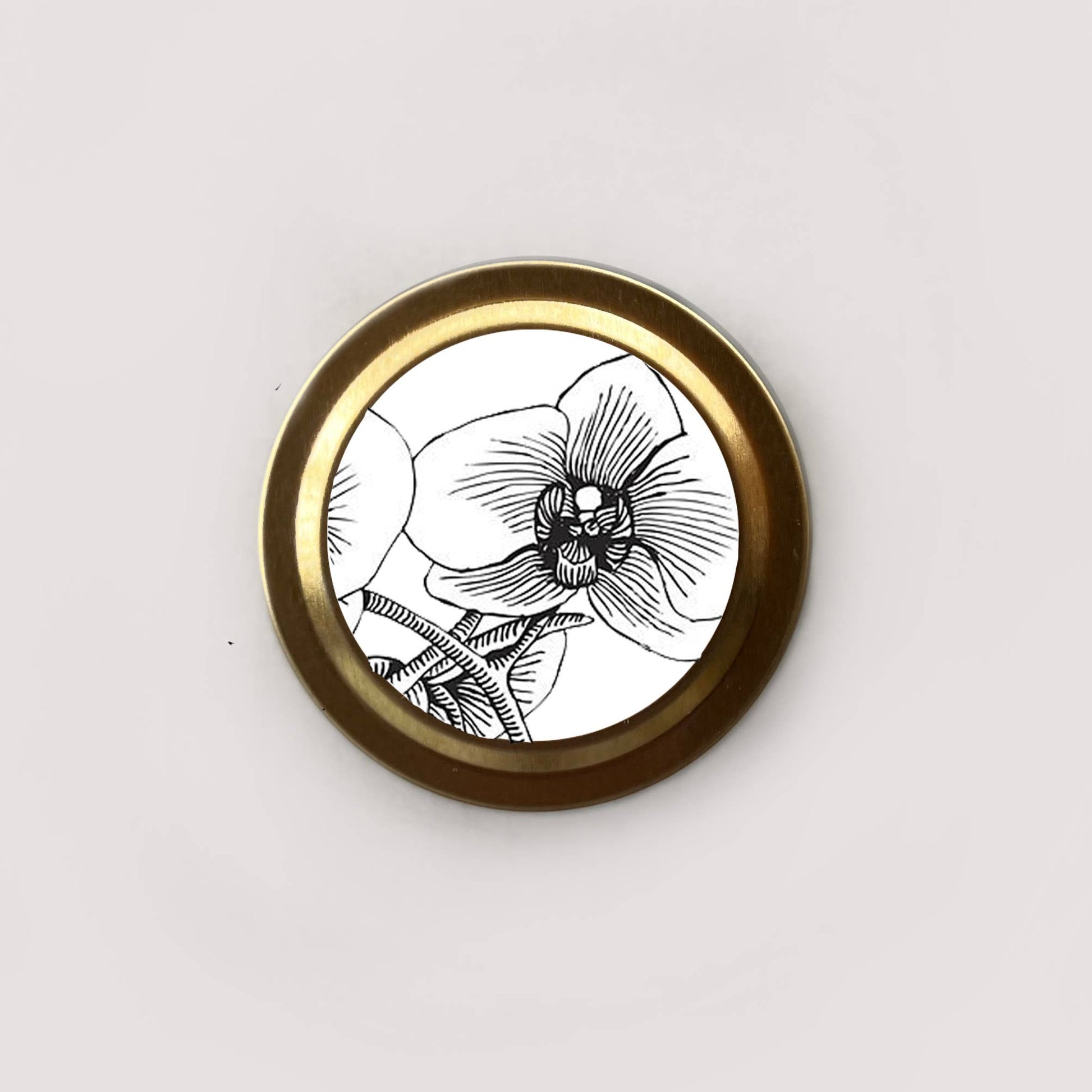 Round brass object with black and white floral design on a light gray background