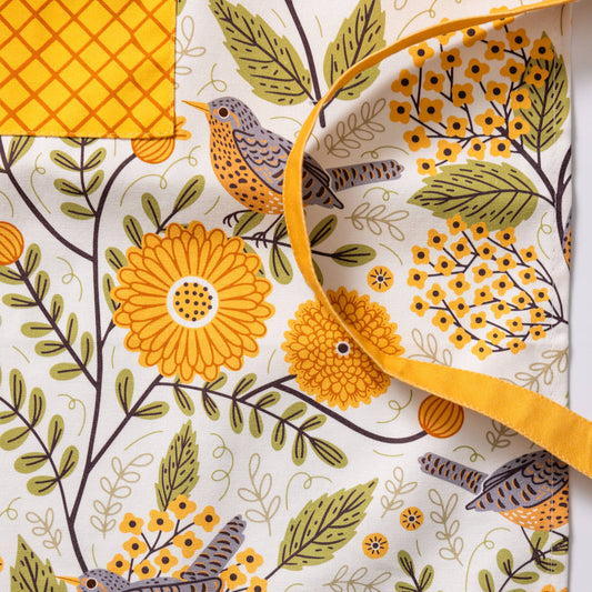 Fabric with floral and bird pattern, featuring yellow flowers and green leaves, with a visible brand label 'GINGER'.