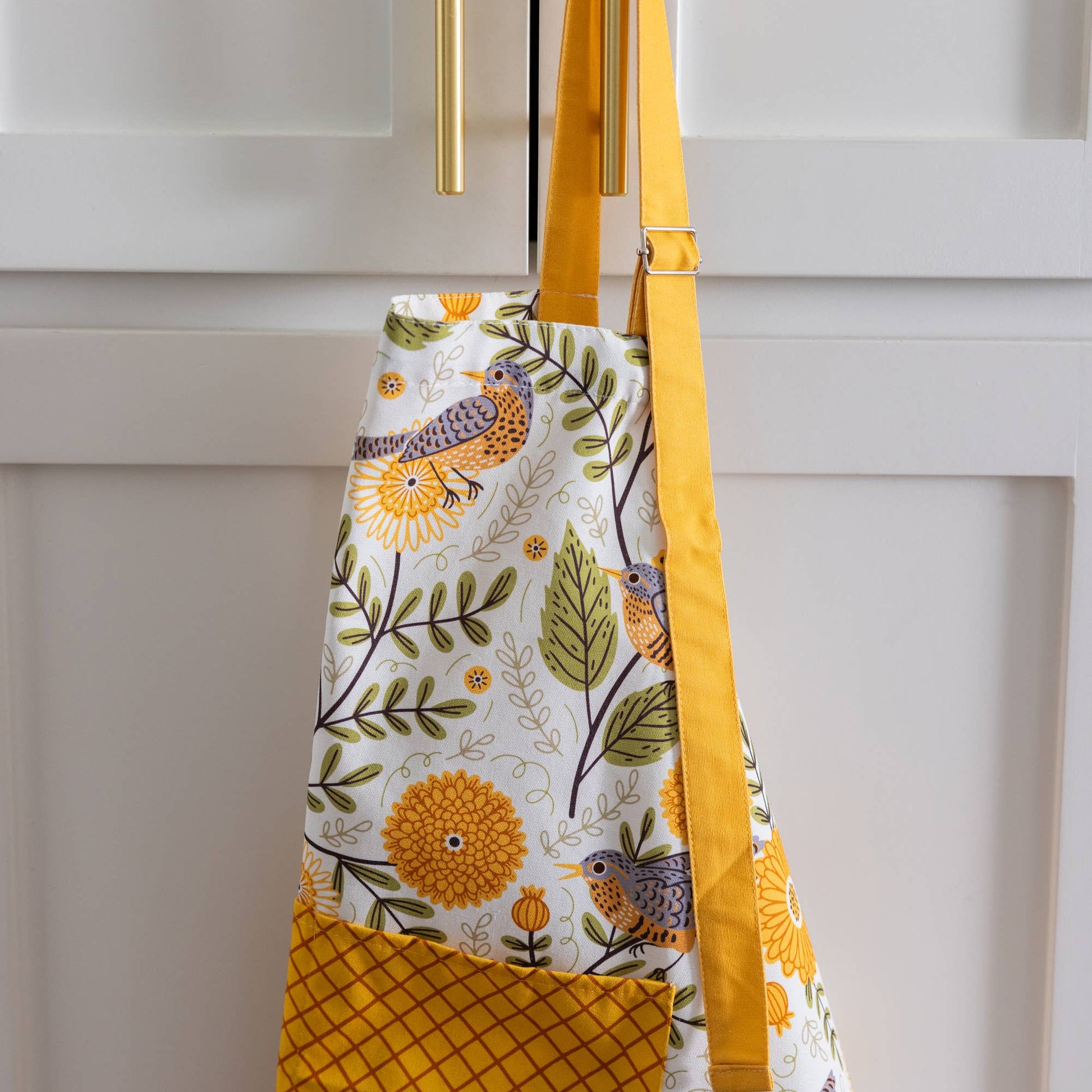 Colorful apron with floral and bird pattern hanging on a cabinet door.
