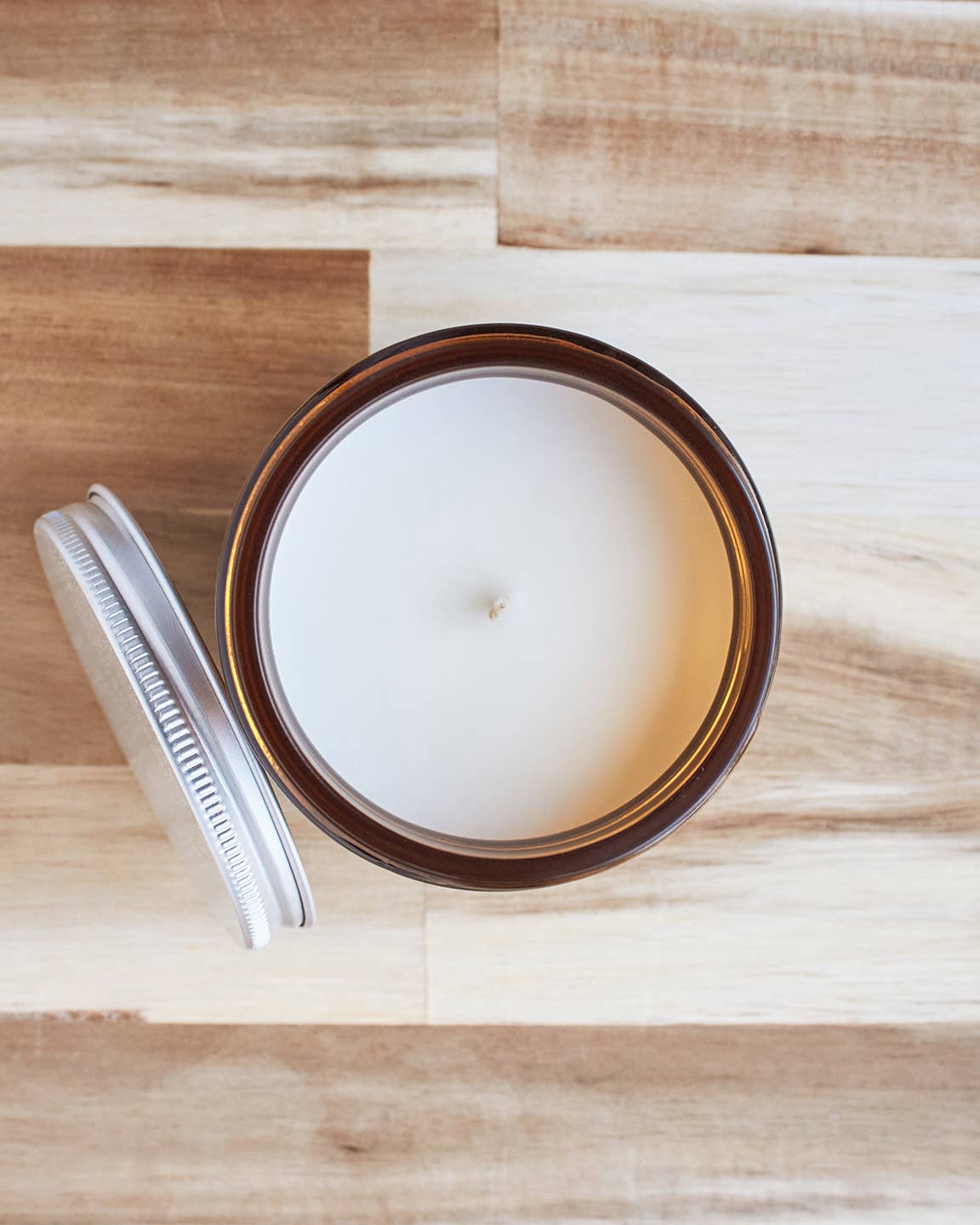 Candle in a brown jar with a white lid on a wooden surface