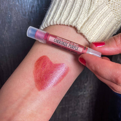 Lined Kewax lip balm labeled 'Cherokee Purple' on a person's arm with a heart-shaped swatch.