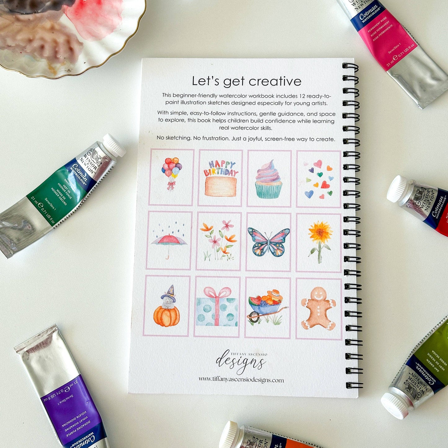 Spiral-bound book titled 'Let's get creative' with paint tubes around on a light background