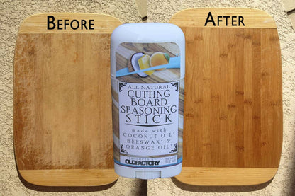 A stick of ClueFactory All Natural Cutting Board Seasoning Stick centered between two wooden cutting boards labeled 'BEFORE' and 'AFTER' on a sandy beige background.