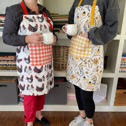 Two people wearing aprons holding white mugs in a kitchen setting.