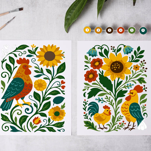 Two colorful illustrations of roosters and flowers on a gray surface with paintbrushes and leaves.