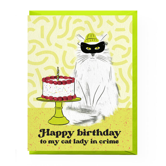 Birthday card with a cat and cake illustration and text 'Happy birthday to my cat lady in crime' on a yellow background.
