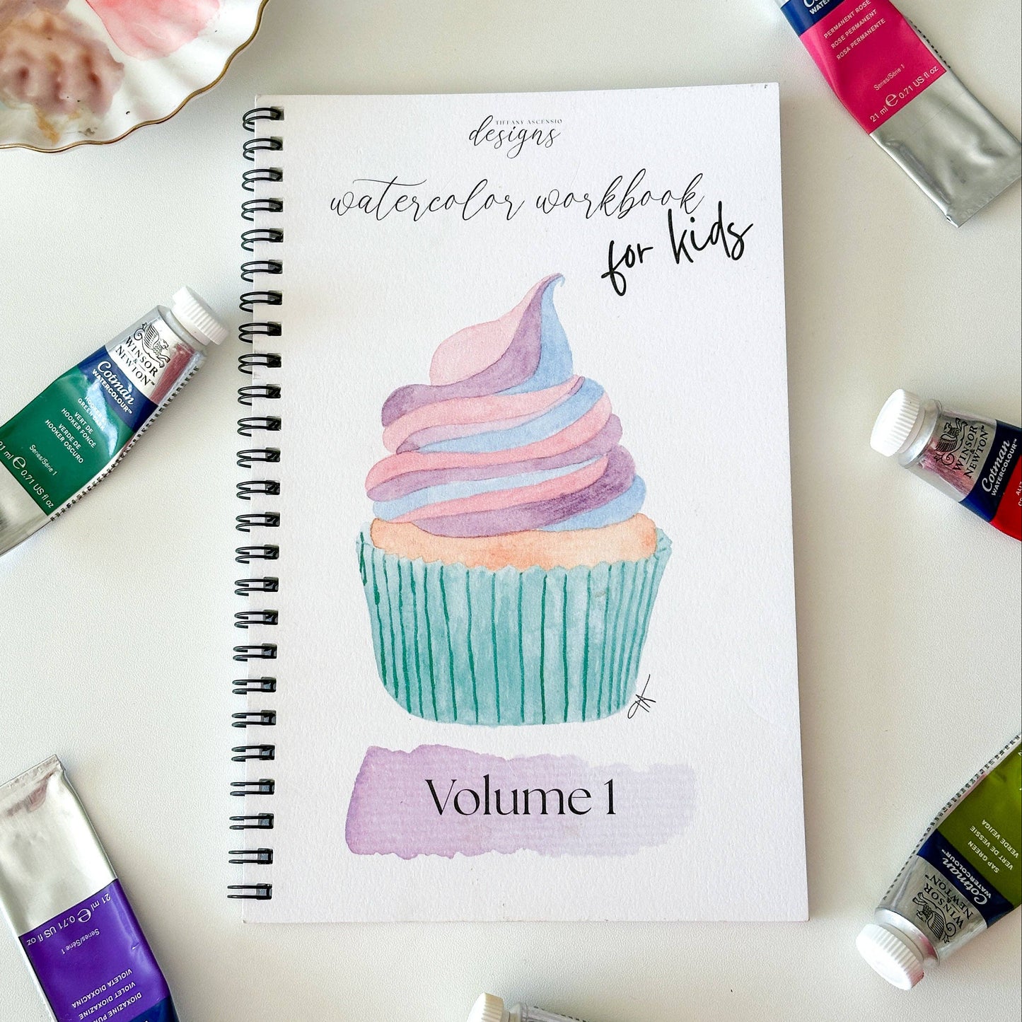 Watercolor workbook for kids with paint tubes on a white surface
