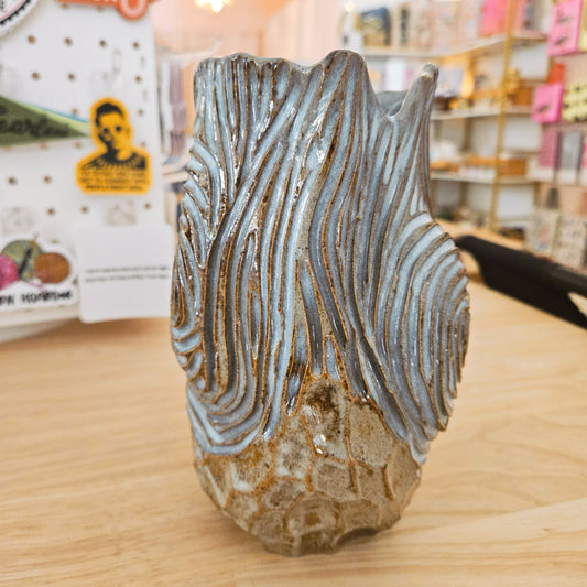 Decorative vase with wavy pattern on a wooden surface in a store setting