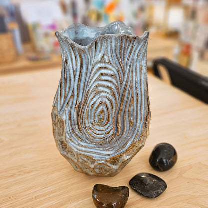 Decorative glass vase with textured design on a wooden surface, surrounded by small stones.