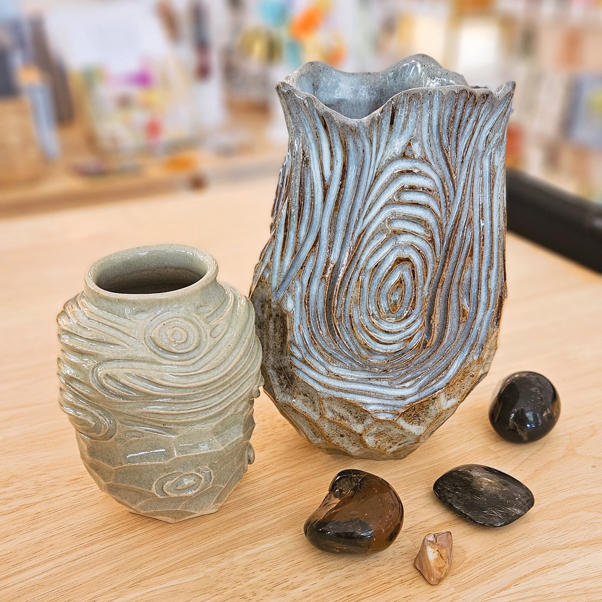 Two ceramic vases on a wooden surface with pebbles and stones.