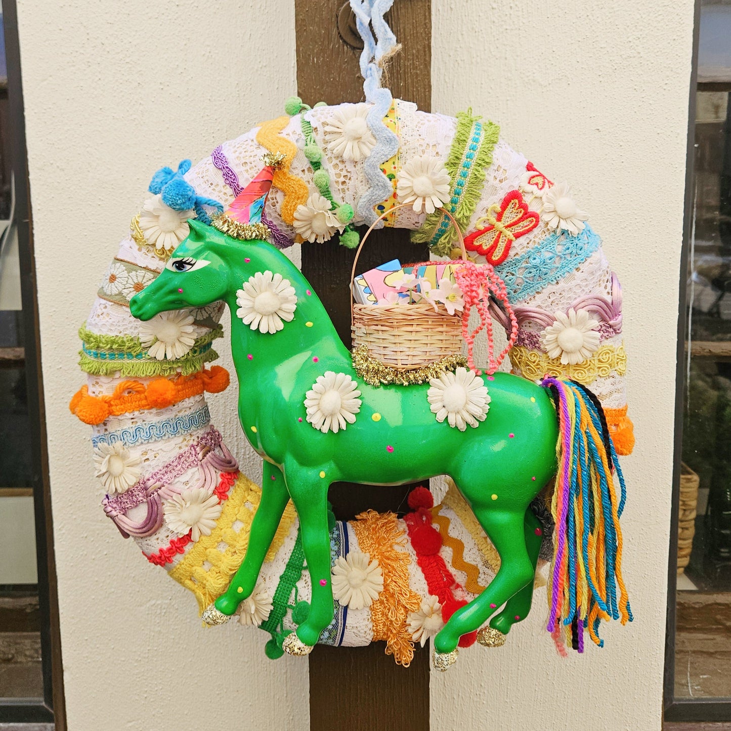 Colorful horse on circular wreath with decorative elements against a neutral wall.