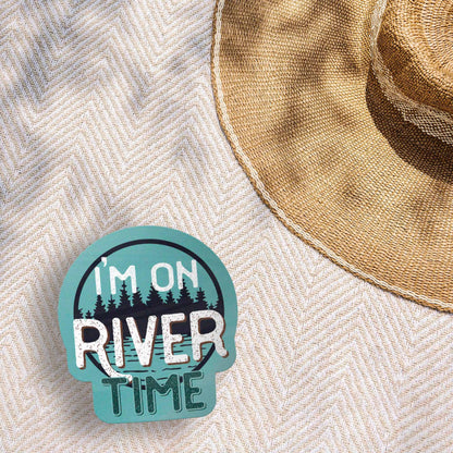 Sticker with 'I'm on River Time' text on a textured surface with a straw hat.