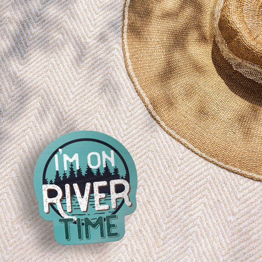 Sticker with 'I'm on River Time' text on a textured surface with a straw hat.