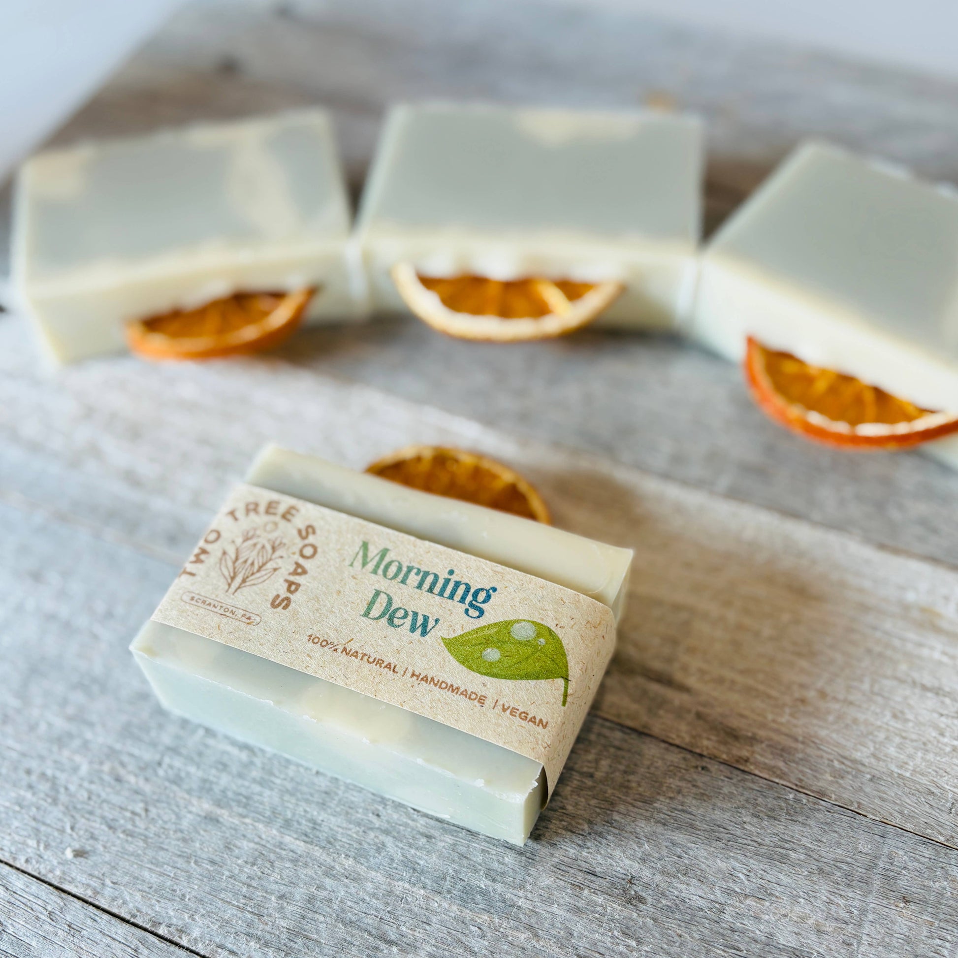Bar of soap with 'Morning Dew' branding on a wooden surface with dried oranges.