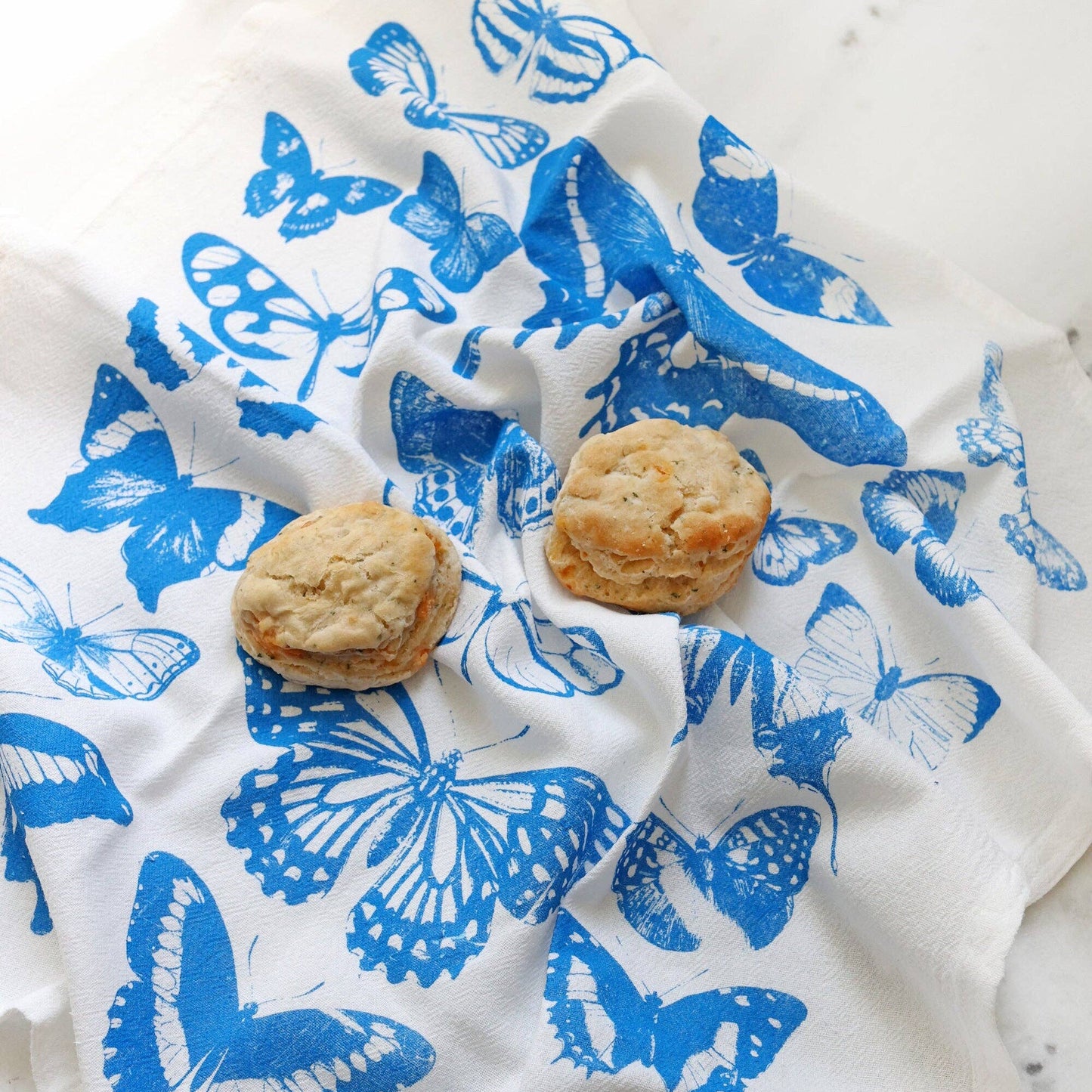 Butterflies on a white towel with two biscuits on a marble surface