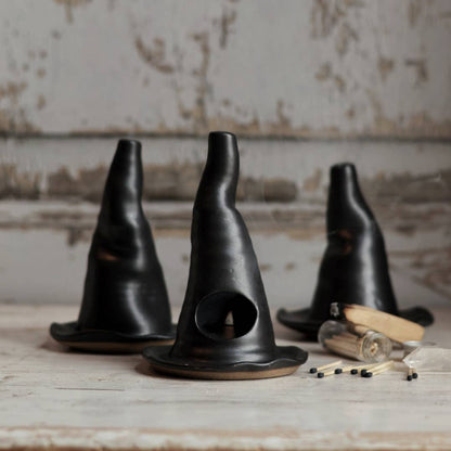 Three black ceramic cones on a rustic wooden surface with a textured wall background.