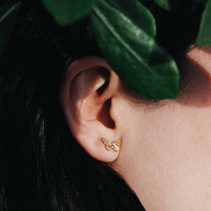 Gold butterfly earring worn by a person with green leaves in the background