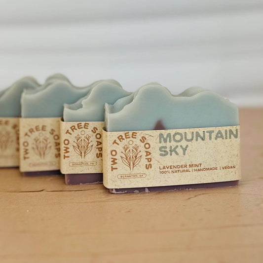 Three bars of soap with 'Two Tree Soaps' branding on a wooden surface.