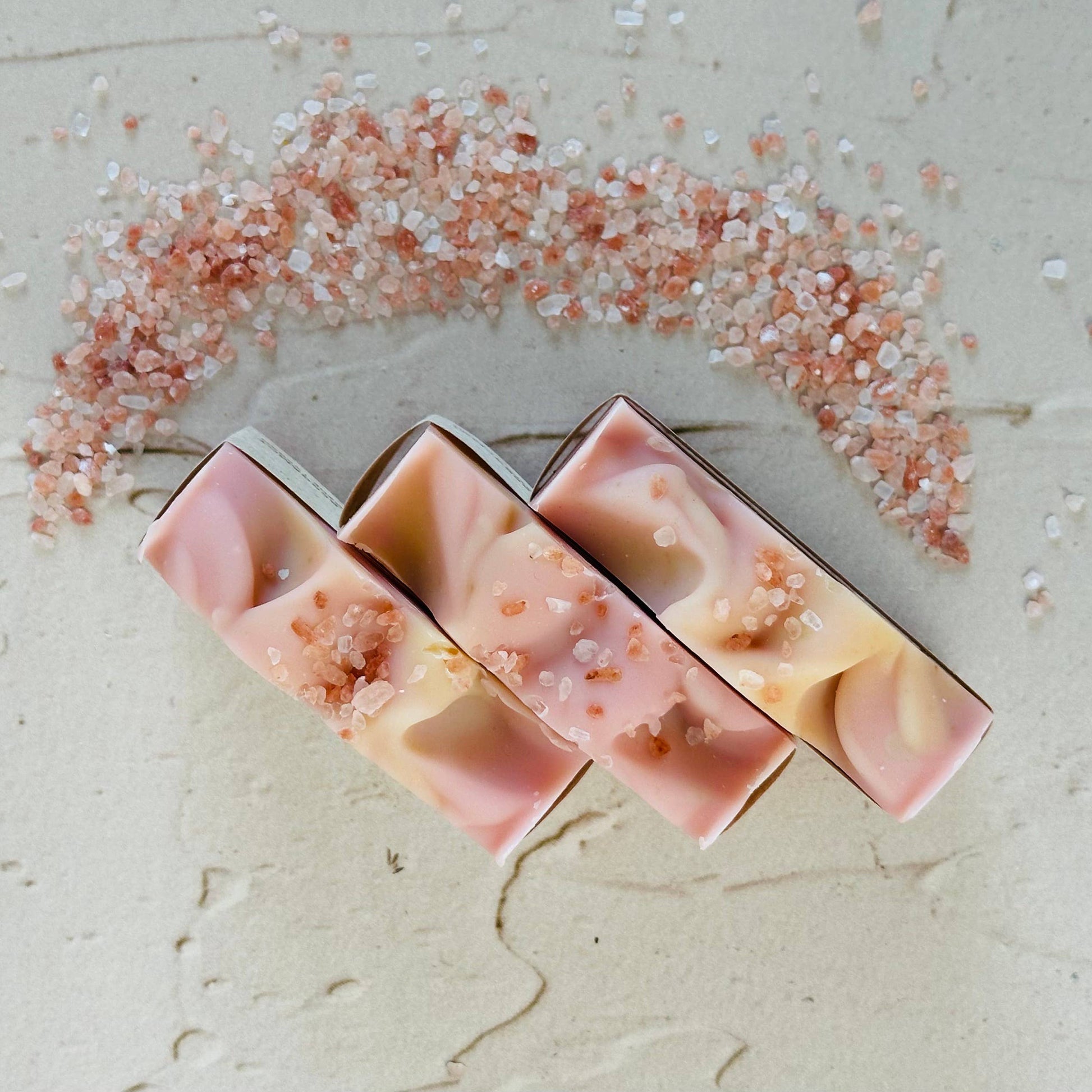 Three pink and beige soap bars with decorative elements on a textured surface.