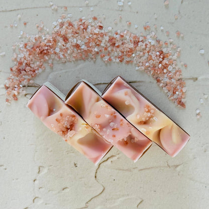 Three pink and beige soap bars with decorative elements on a textured surface.