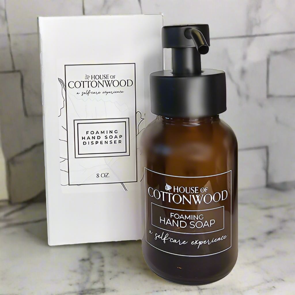 Brown foaming hand soap dispenser with black pump and 'House of Cottonwood' branding on a marble surface.