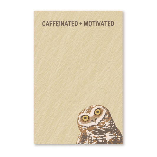 A rectangular notepad with a textured beige cover, printed with the phrase 'CAFFEINATED + MOTIVATED' at the top and featuring a painted owl at the bottom right, shown on a white background.