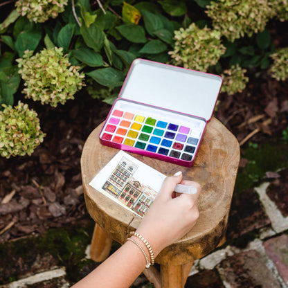 Person drawing with watercolors on a small stool outdoors
