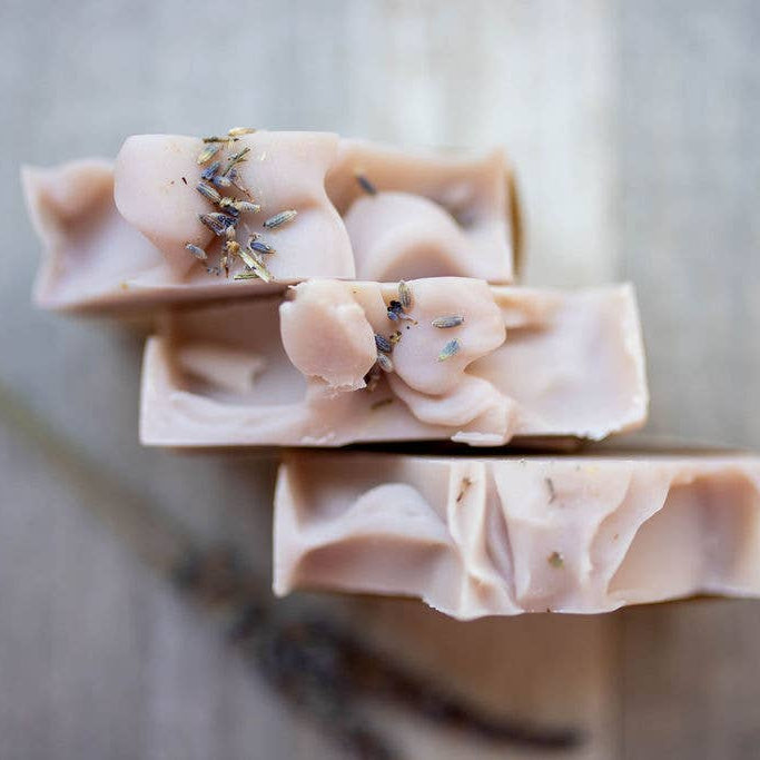Three bars of soap with lavender buds on a wooden surface