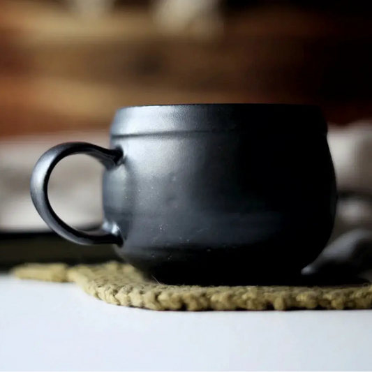 Black ceramic mug on a textured surface with a blurred background
