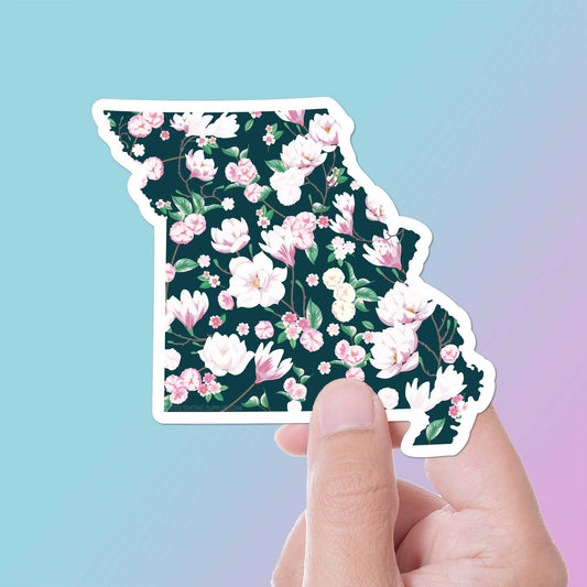 Floral-patterned state-shaped sticker held by a hand against a gradient background