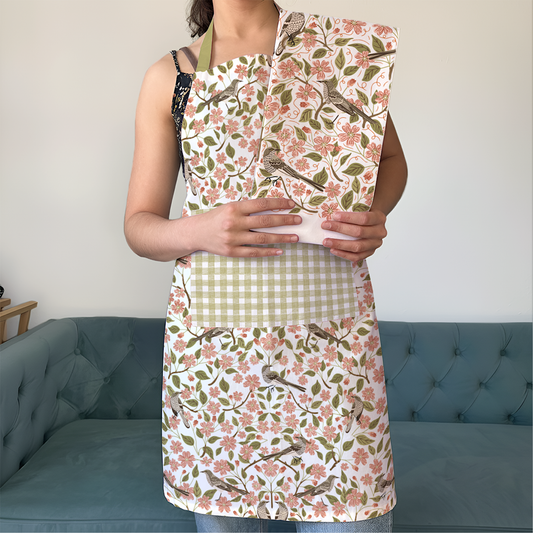 Person wearing a floral apron holding a patterned book against a neutral background.