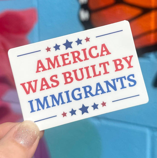 Card with 'America was built by immigrants' text held by a hand against a colorful background