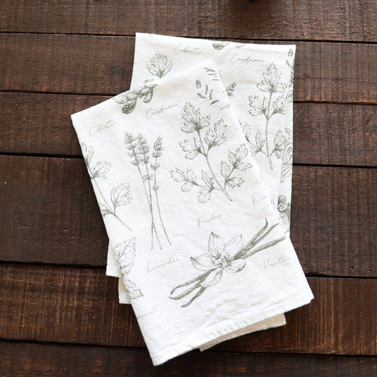 Floral-patterned tea towels on a wooden surface with a lit candle and tea packages.