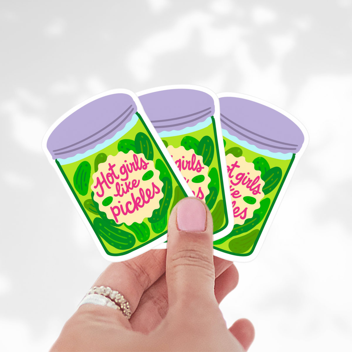 Three 'Hot girls like pickles' stickers held by a hand against a white background