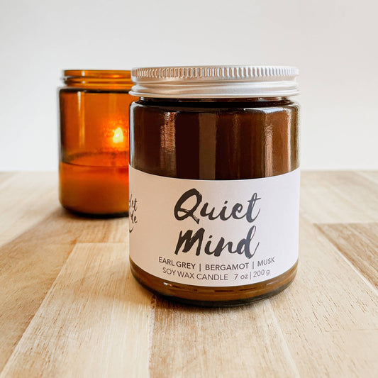 Candle jar labeled 'Quiet Mind' on a wooden surface with another candle in the background.