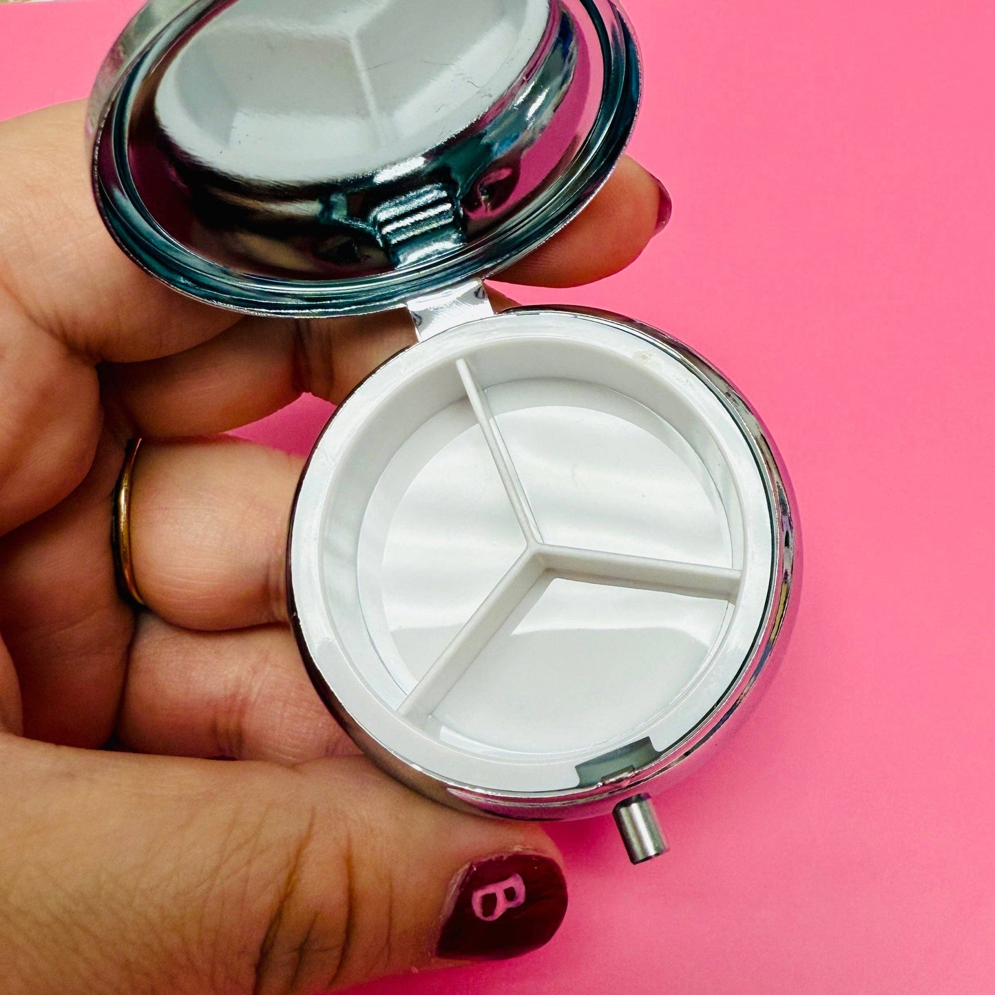 Hand holding a small round mirror with a pink background