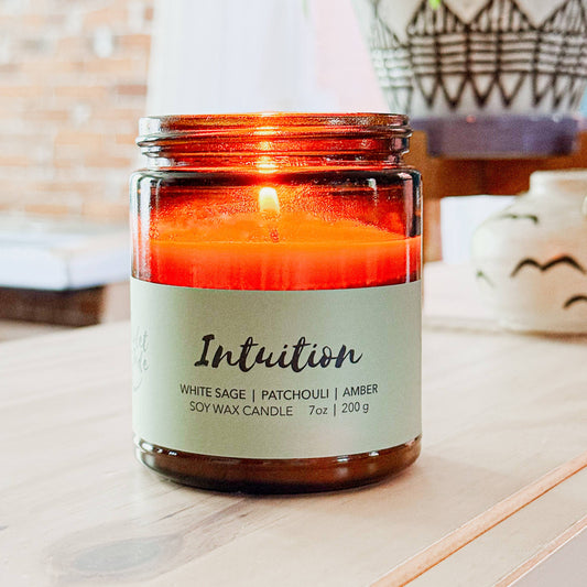 Candle in an amber jar labeled 'Intuition' on a wooden surface.