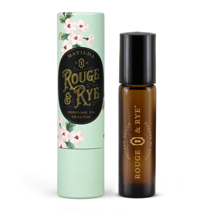 Matilda Rouge & Rye perfume oil shown with its mint green floral cardboard packaging tube and the amber glass bottle with a black cap on a white background.