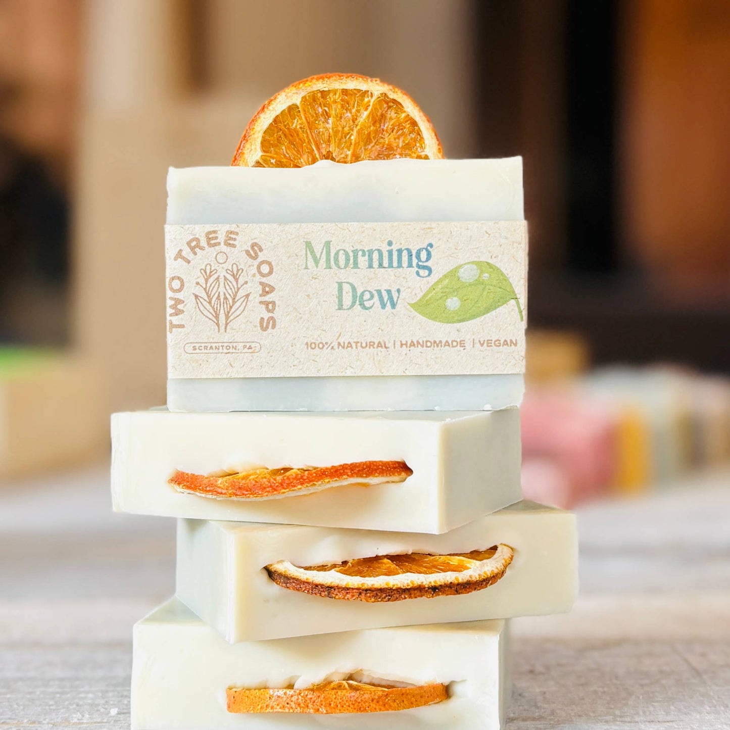 Three bars of soap stacked on a marble surface with orange slices, featuring 'Two Tree Farms' branding.