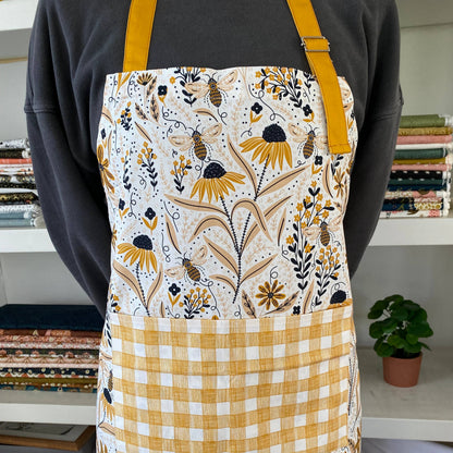 Person wearing a floral apron with yellow accents in a room with books and a plant.
