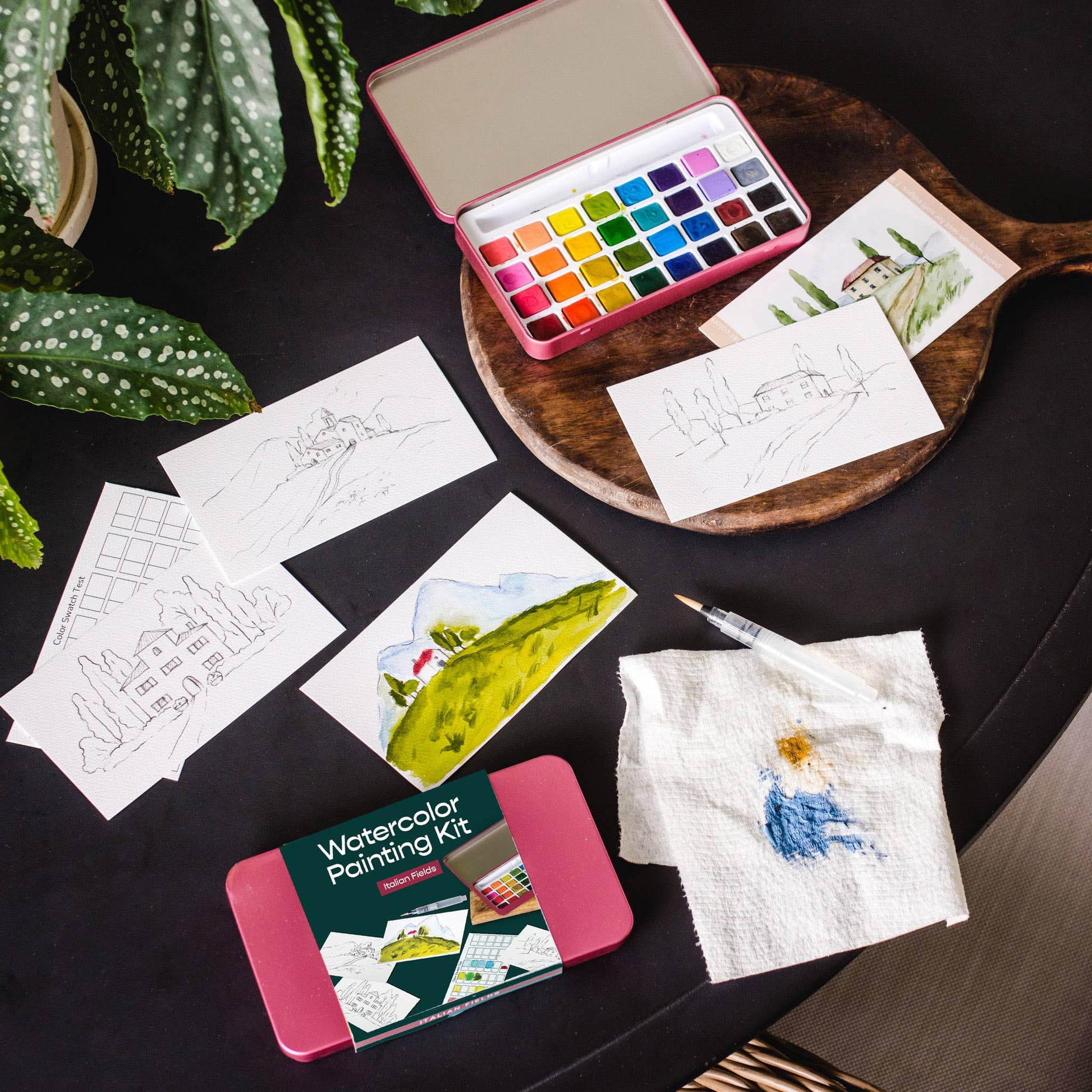 Watercolor painting kit with paint, brushes, and samples on a dark surface.